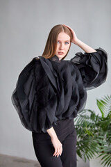 A beautiful woman in a stylish black dress, with long hair and flawless makeup, poses in front of the camera in a professional studio.