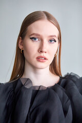 A beautiful woman in a stylish black dress, with long hair and flawless makeup, poses in front of the camera in a professional studio.