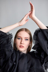 A beautiful woman in a stylish black dress, with long hair and flawless makeup, poses in front of the camera in a professional studio.