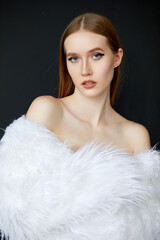 Portrait of a woman, taken in close-up. She is wearing a long white fur coat, and her hair is a chestnut shade.