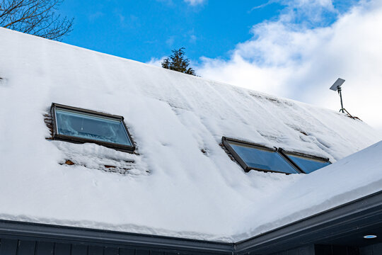 Snow-covered roof with skylight windows on modern house exterior in winter