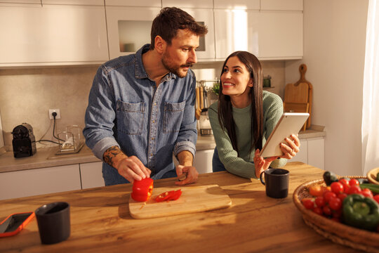 Couple using tablet computer while cooking meal together in the kitchen at home - Powered by Adobe
