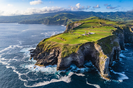 Rugged Atlantic cliffs with the Cintrao lighthouse set above green coastal land, aerial view - Powered by Adobe