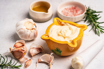 Homemade aioli or allioli garlic sauce in a special mortar on a table with the pestle on the side and ingredients the garlic, olive oil and salt