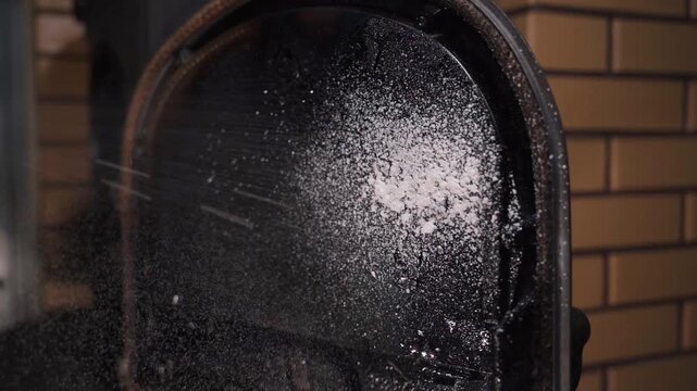 The window of the fireplace stove covered in black soot is sprayed with detergent, close-up
