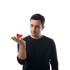 A pensive man holds a small red object in his hand, looking at it with a contemplative and curious expression on an isolated background