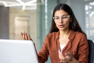Young businesswoman with clear glasses actively participating in an online video call meeting. Communicating and discussing business strategies while working remotely from a modern office environment