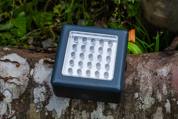 Rectangular LED light panel with 25 bulbs placed on tree trunk outdoors.