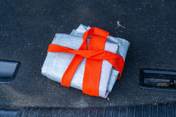 Tightly wrapped package with orange strap placed on carpeted vehicle floor.