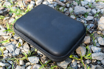 Black zippered hard case placed on rocky ground with small green plants.