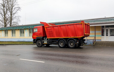 Dump truck sits on the side of the road. Construction equipment is parked near a one-story building.