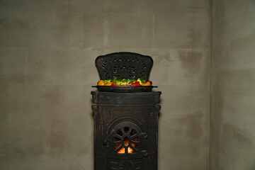 Grilled meat and mixed vegetables cooking in cast iron pan on wood burning stove. Indoor food preparation photography. Home cooking and rustic kitchen concept. Design for poster, banner, wallpaper, pr