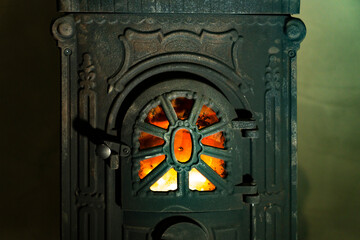 Cast iron wood burning stove door with visible fire flame behind metal grate. Indoor heating appliance close up photography. Home heating and solid fuel stove concept.