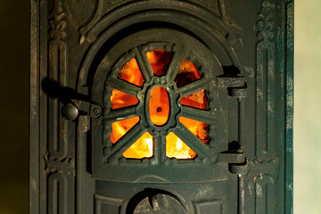 Cast iron wood burning stove door with visible fire flame behind metal grate. Indoor heating appliance close up photography. Home heating and solid fuel stove concept.