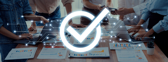 A dynamic office scene showing professionals collaborating around a table with charts and devices, highlighted by a digital checkmark symbolizing success and completion. Trope