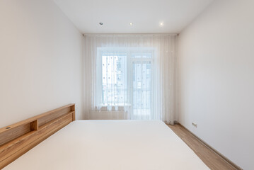 Minimalist Home Bedroom With White Walls, Wooden Bed, and Bright Natural Light