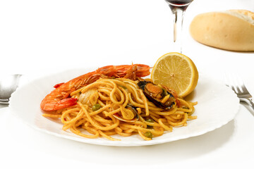 Gourmet seafood spaghetti with shrimp and mussels served on a white plate with lemon, bread and red wine. Elegant Italian Mediterranean cuisine in studio setting.