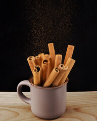 cinnamon sticks in a cup on a wooden board on a black background, close-up