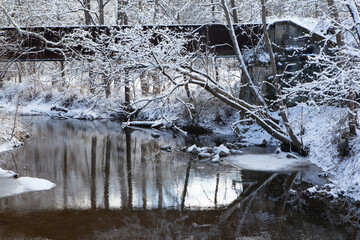 A snow-covered creek reflects bare winter trees beneath an old bridge.