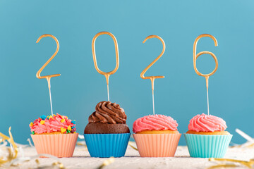 Holiday New Year muffins with pink butter cream and 2026 numbers on blue background.