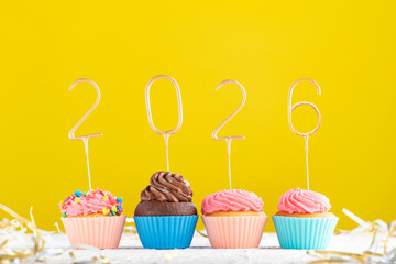 Homemade muffins decorated with 2026 numbers on yellow background. Happy New Year, Merry Christmas concept.