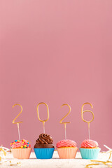 Cupcakes or muffins with buttercream frosting decorated with gold 2026 numbers on pink background. Vertical frame