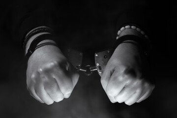 Hands in handcuffs, gripping tightly, surrounded by a smoky atmosphere, conveying themes of confinement, struggle, and the complexities of justice and freedom in a dramatic monochrome setting