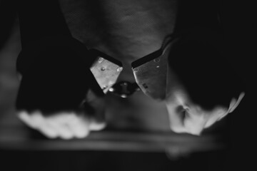 Hands gripping metal handcuffs in a dramatic black and white setting, emphasizing tension and restraint, capturing the essence of law enforcement and justice themes