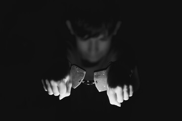 Young boy with hands in handcuffs, illuminated against a dark background, conveying themes of confinement, innocence, and the impact of crime on youth in a dramatic visual narrative