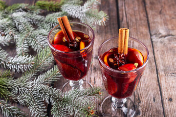 Mulled wine. Festive mulled wine served in elegant glasses, garnished with cinnamon sticks and fruits, surrounded by evergreen branches on rustic wooden table, creating warm holiday atmosphere