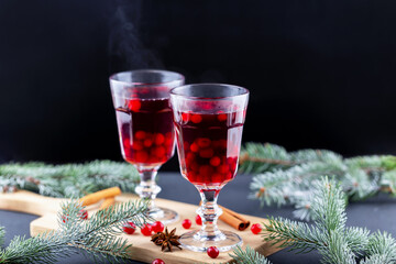 Mulled wine. Festive holiday drinks served in elegant glasses, filled with cranberries, placed on wooden board surrounded by fresh pine branches, creating warm and inviting atmosphere for celebrations