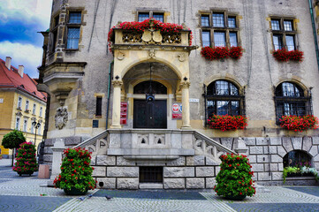 Historyczne wejście do ratusza z kamiennymi schodami, łukiem i balkonami w czerwonych kwiatach. Miasto Jawor – zabytkowy ratusz na Starym Mieście. © Pol Badger