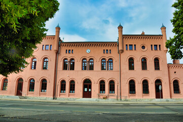 Różowy, zabytkowy budynek dworca kolejowego w Jaworze (w stylu neoromańskim) z łukowymi oknami i ceglaną fasadą tworzy miejską scenerię kolejową. © Pol Badger