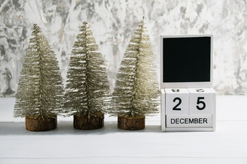 Decorative Christmas trees on a gray background and a wooden calendar with the date December 25