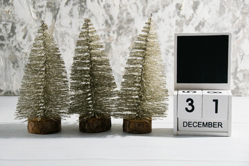 Decorative Christmas trees on a gray background and a wooden calendar with the date December 31