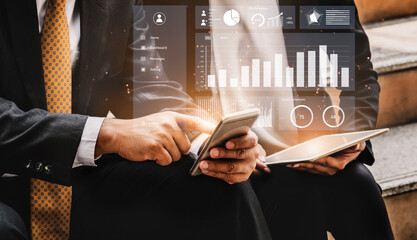 Two business professionals engage in data analysis using a smartphone and tablet, displaying financial graphs and statistics in a contemporary office environment. Impute