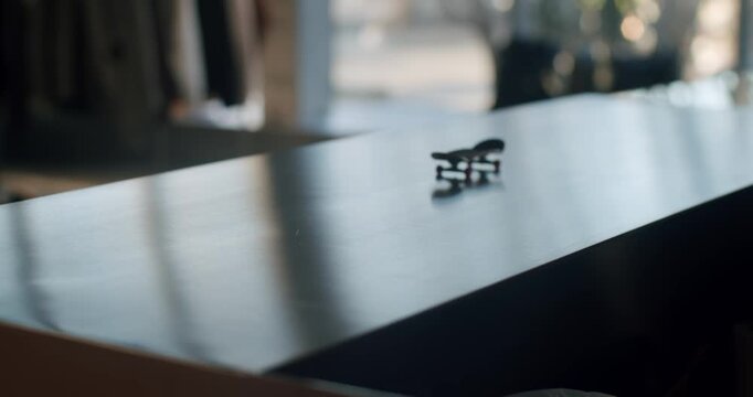 Close up of a fingerboard on a table in a board shop. A hand skillfully performs tricks with the miniature skateboard, showcasing its versatility and maneuverability.