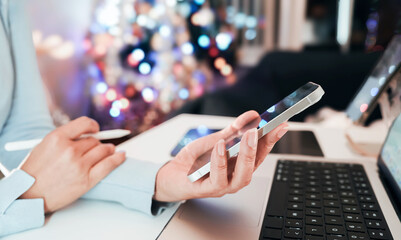 Woman using smartphone and digital pen on tablet near laptop during holiday season. Remote work or...