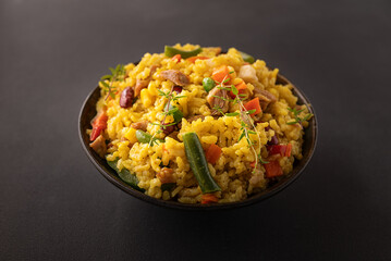 Stewed rice with meat and assortment on vegetables and spices in dark ceramic bowl on black stone table close up. Tasty homemade food concept.