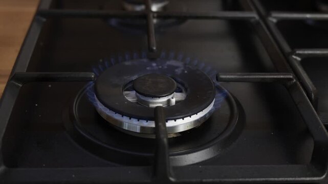 A gas burner lights up with a blue flame on a stovetop for cooking food
