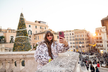 Woman taking a festive selfie overlooking Rome near the Spanish Steps with a decorated Christmas tree and lively city square. Holiday atmosphere, winter tourism, city break travel and European