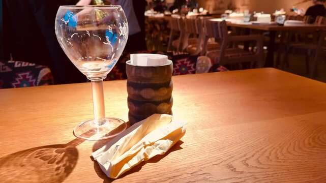 Wine glass stacked cookies wafer on wooden table, warm amber lighting casts elongated shadow, patterned upholstery background, clear glass reflection and rustic texture create
