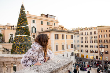Woman enjoying a festive winter moment overlooking Rome near the Spanish Steps with a decorated Christmas tree and lively city square. Holiday atmosphere, winter tourism, city break travel and