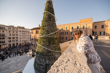 Smiling woman enjoying a festive moment near a decorated Christmas tree overlooking Rome by the Spanish Steps. Holiday atmosphere, winter tourism, city break travel, joy, freedom and European