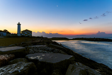 Sunrise at Bibione lighthouse on the Adriatic coast of Italy with calm sea, rocky breakwater and pastel sky, peaceful coastal landscape, travel destination, freedom, relaxation, maritime background
