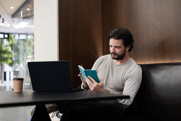 Young startup founder reading notes while working on a laptop in a modern coworking space. Concept of business strategy, SaaS, IT planning and digital work