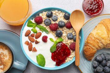 Healthy breakfast. Oatmeal with nuts, berries, yoghurt, jam, croissant, coffee and juice on grey textured table, flat lay