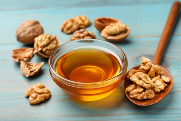Honey in bowl and walnuts on light blue wooden table, closeup