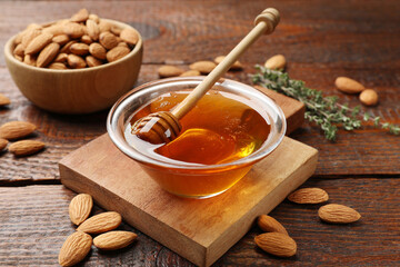 Honey in bowl, dipper and almonds on wooden table, closeup