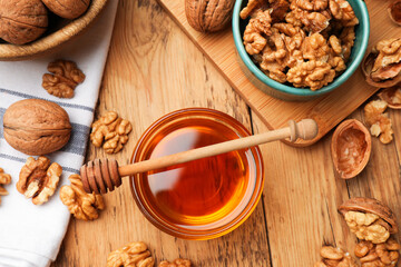 Obraz premium Delicious honey in glass bowl, dipper and walnuts on wooden table, flat lay